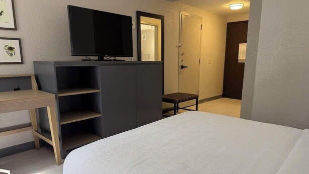 A hotel room with a bed, a desk, a television, and a door leading to a bathroom. - Wingate by Wyndham Jacksonville FL (Jacksonville)