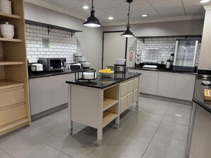 A modern kitchen with a central island, black countertops, white cabinets, and a tiled backsplash. - Wingate by Wyndham Jacksonville FL (Jacksonville)