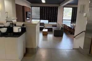A modern kitchen with white cabinets and black countertops, a dining area with a sofa and table, and large windows with blinds. - Wingate by Wyndham Jacksonville FL (Jacksonville)