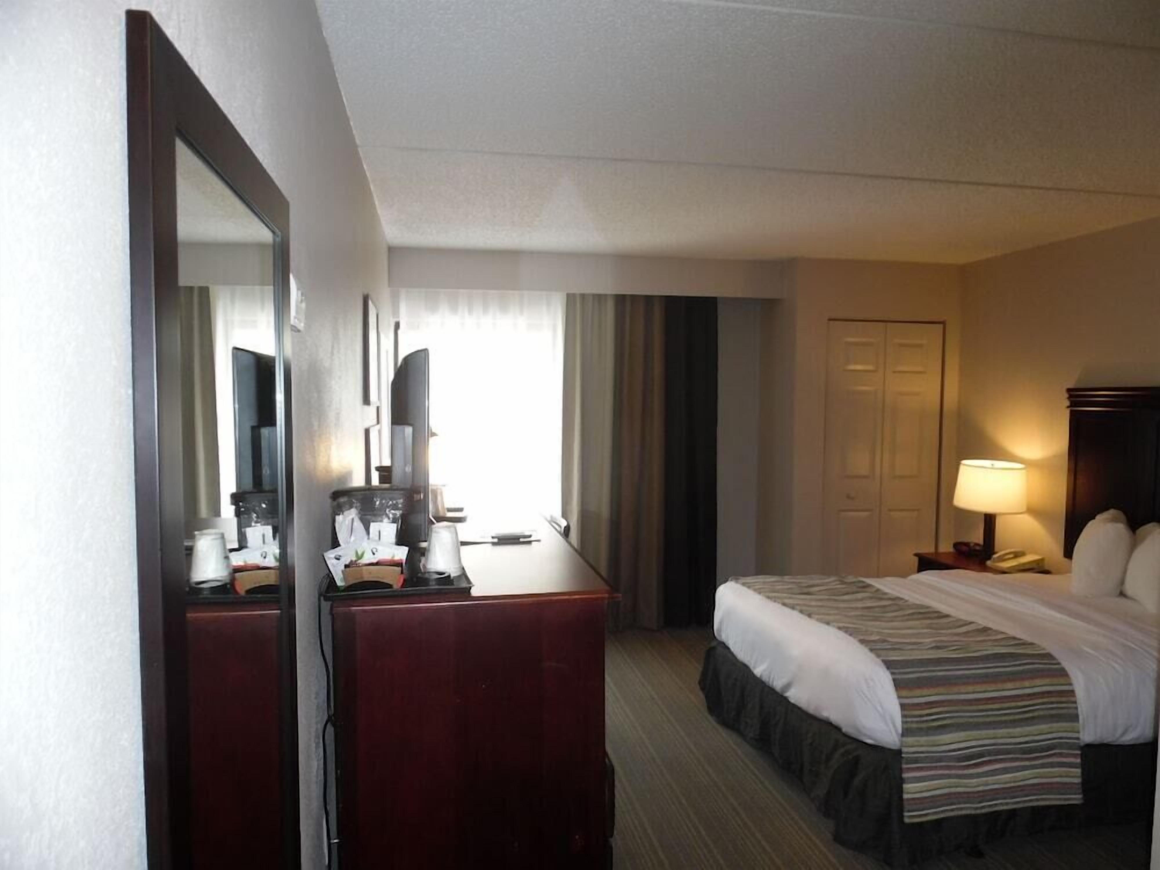 A hotel room with a bed, a desk, a mirror, a lamp, and a door.