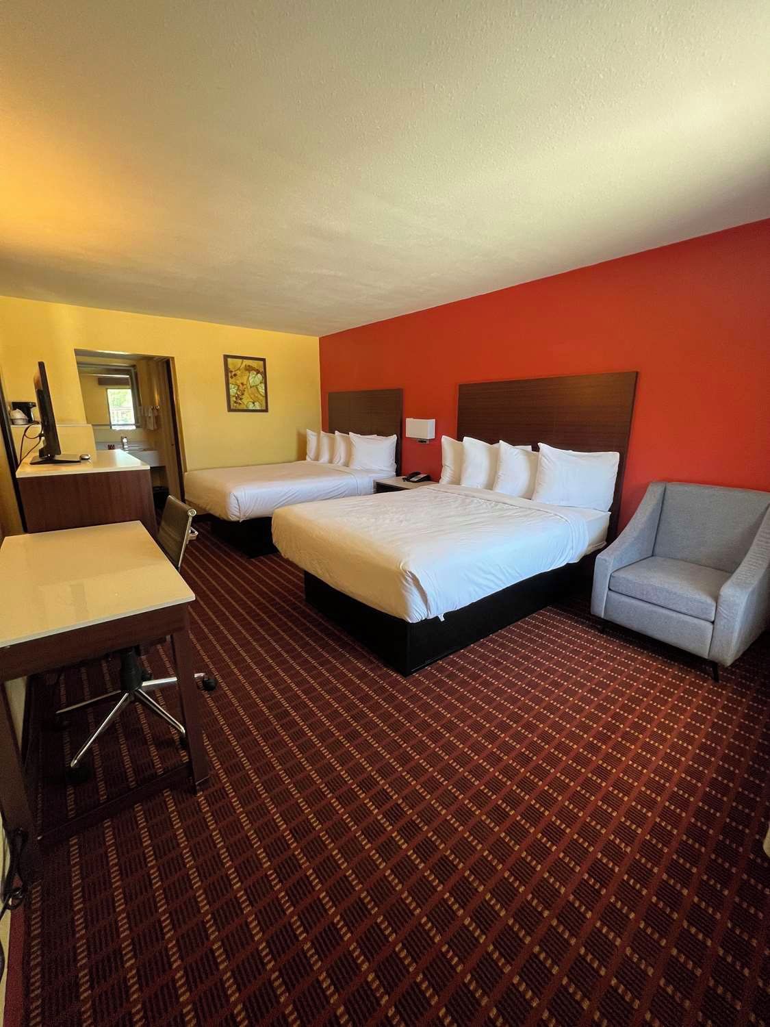 Habitación de hotel con dos camas, un escritorio, una silla y suelo alfombrado.