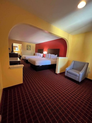 A hotel room with a red accent wall, a large bed, a chair, and a carpeted floor.