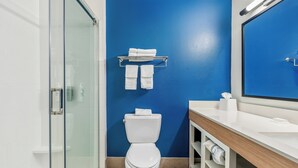 A bathroom with a glass shower enclosure, a white toilet, a blue wall, and a white sink with a mirror.