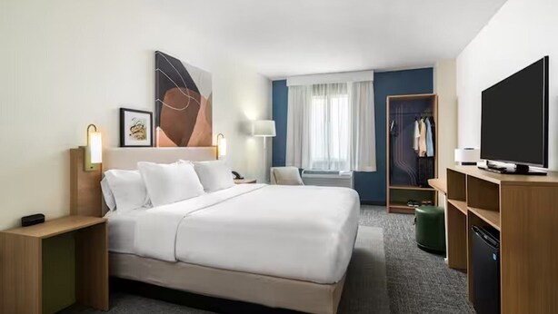 A hotel room with a large bed, bedside tables, a TV, a wardrobe, and a window with curtains.