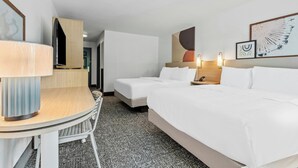 A hotel room with a desk, two beds, a chair, and a carpeted floor.