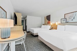 Habitación de hotel con escritorio, dos camas, una silla y piso alfombrado.