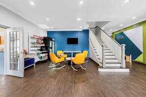 A modern interior with a dining area, a staircase, and a wall-mounted TV. - Spark by Hilton St. Augustine I 95 (St. Augustine)
