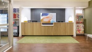 A reception area with a wooden reception desk, a large abstract painting above it, and shelves stocked with various items on either side.