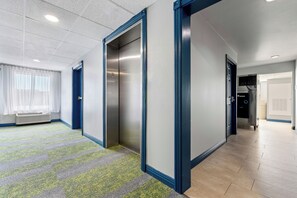 A hallway with a carpeted floor, a radiator, and a door with a number plate. - Spark by Hilton St. Augustine I 95 (St. Augustine)