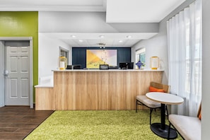Una recepción con un fondo de madera, un área de descanso con una mesa redonda y una alfombra estampada verde.