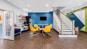 Un interior moderno con una pared azul acentuada, una escalera, un comedor con sillas amarillas y un refrigerador lleno de bocadillos.