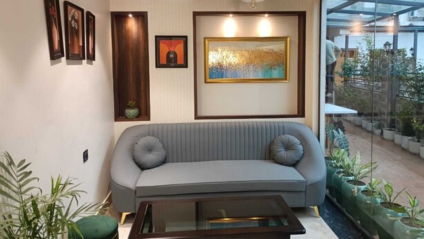 A modern living room with a grey sofa, a glass coffee table, and framed artwork on the wall. - Manyavar Guest House (Deoghar)