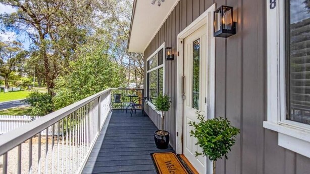 A covered porch with a welcome mat, potted plants, and a small table with chairs.