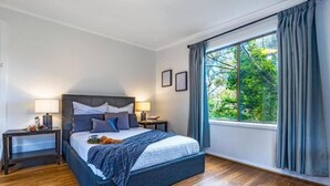A bedroom with a large bed, bedside tables, a window with curtains, and a view of greenery outside.