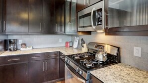 Una cocina moderna con gabinetes oscuros, un microondas de acero inoxidable, una estufa a gas y una cafetera.
