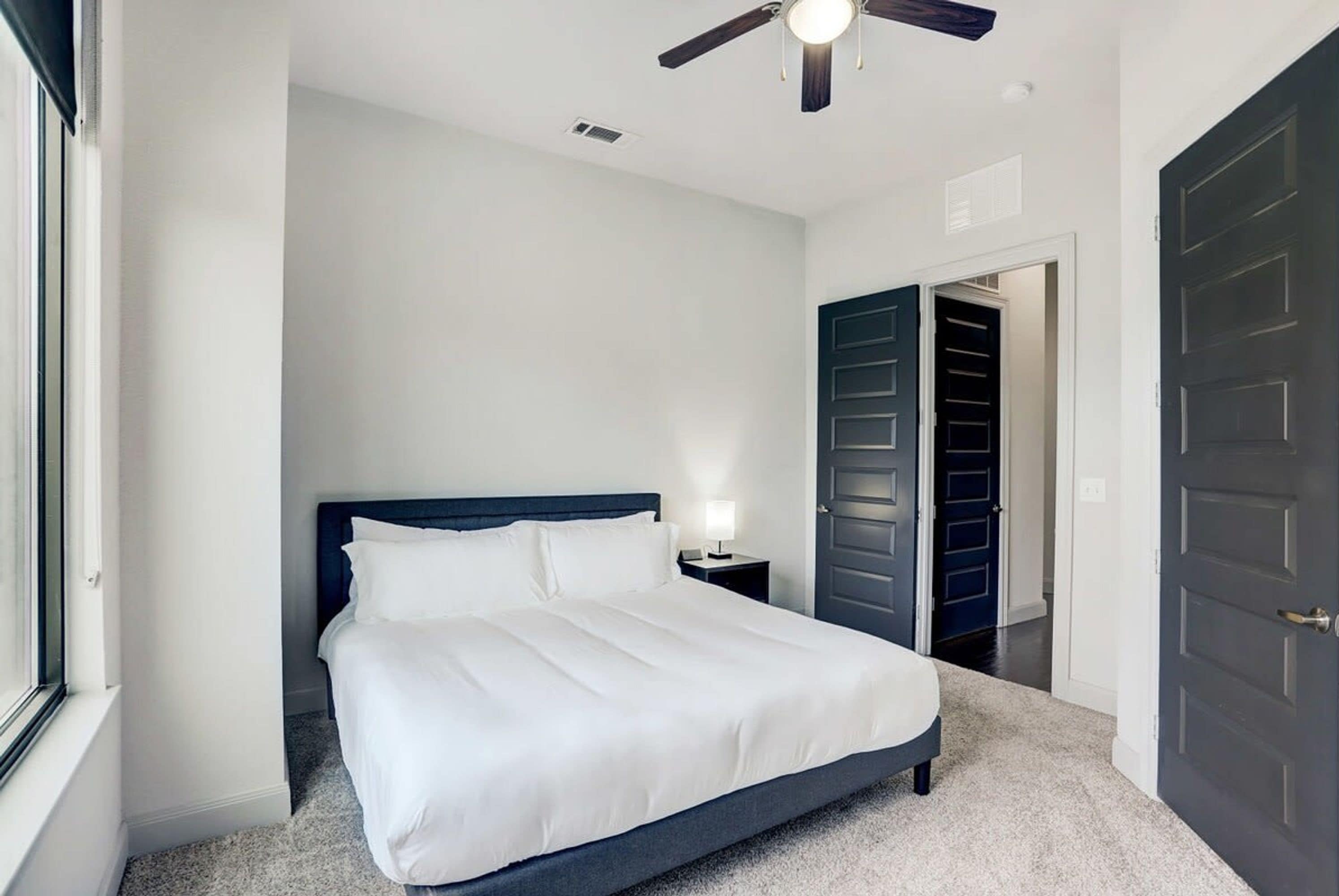 Une chambre à coucher comprenant un lit, une table de chevet, un ventilateur de plafond et une porte donnant sur un placard.