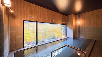 A modern indoor pool area with a view of a bamboo fence and trees outside.