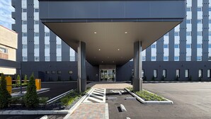Una entrada moderna de edificio con un paseo techado, un estacionamiento y un camino de ladrillo que conduce a la entrada.