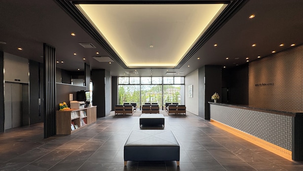 Un moderno vestíbulo de hotel con una zona de estar central, una mesa de recepción y un amplio ventanal con vistas al exterior.
