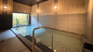 Piscina interior moderna con barrera de cristal, paredes de madera y vistas a zonas verdes.