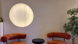 Et moderne venteområde med to komfortable lænestole, et rundt bord og en stor, oplyst vægdekoration.