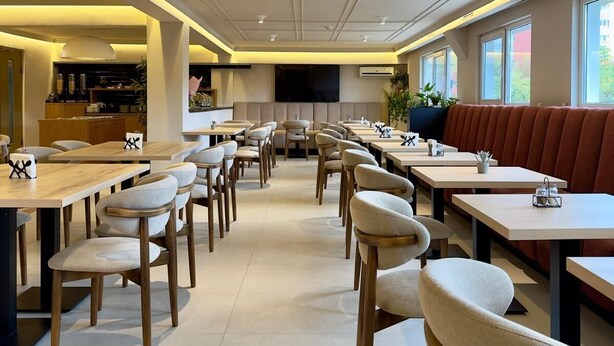 En rummelig restaurant med højt til loftet, moderne belysning og forskellige siddepladser, herunder borde og båse.