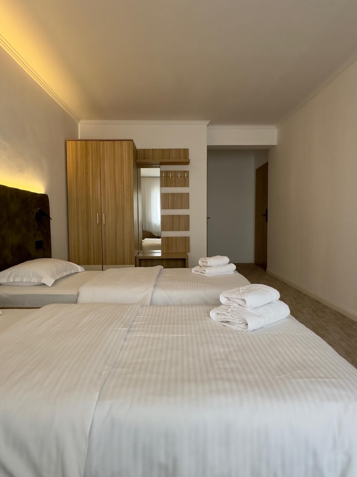 Une chambre d’hôtel avec deux lits, une armoire en bois, un miroir et une petite table avec des serviettes.