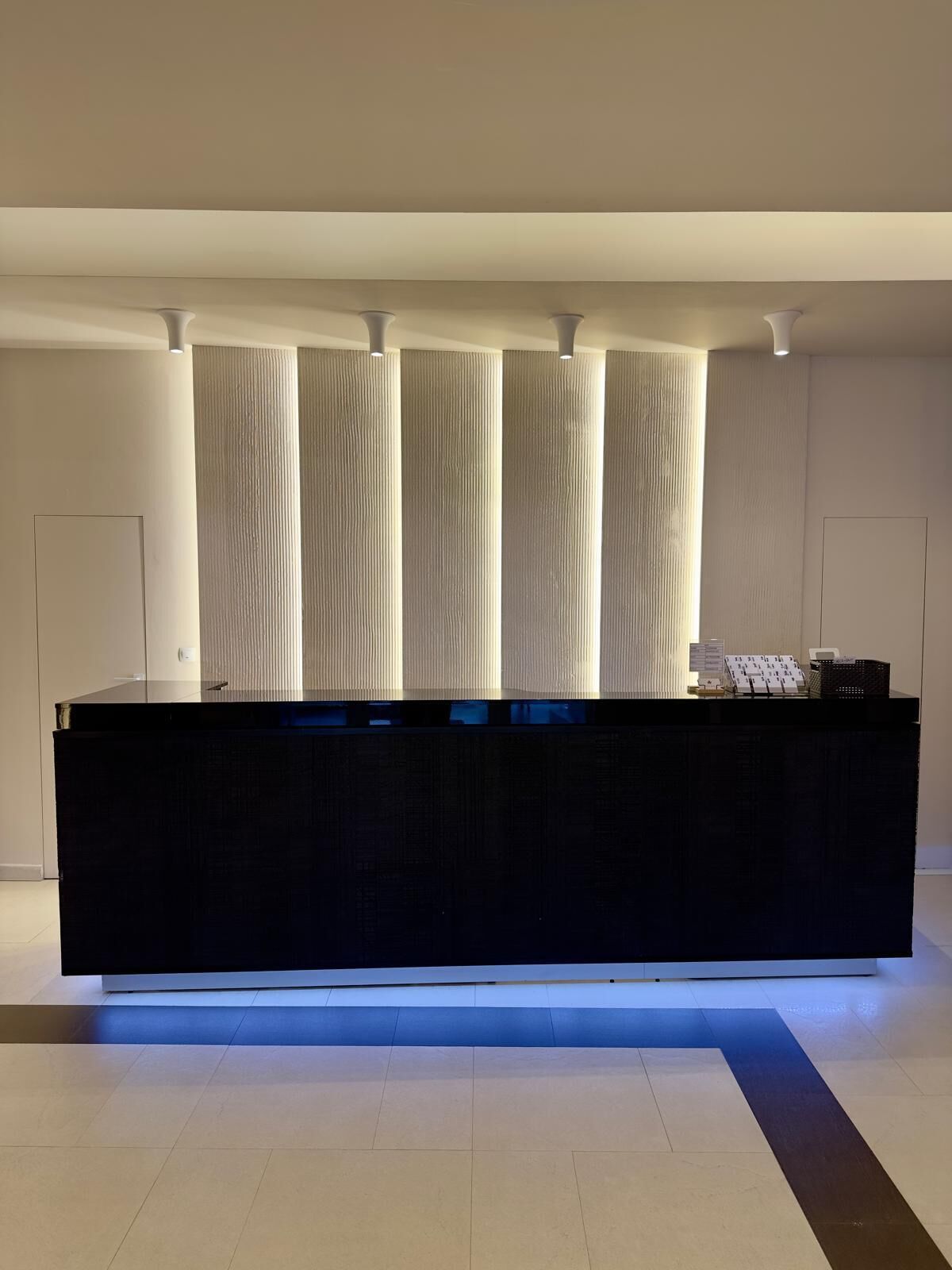 A reception desk with a black surface and a blue-lit base. Behind the desk, there are vertical panels with a textured pattern.