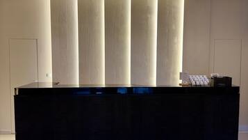 A reception desk with a black surface and a blue-lit base. Behind the desk, there are vertical panels with a textured pattern.