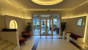 En rummelig lobby med en central, rund lampe, en trappe til venstre og siddeområder på begge sider.
