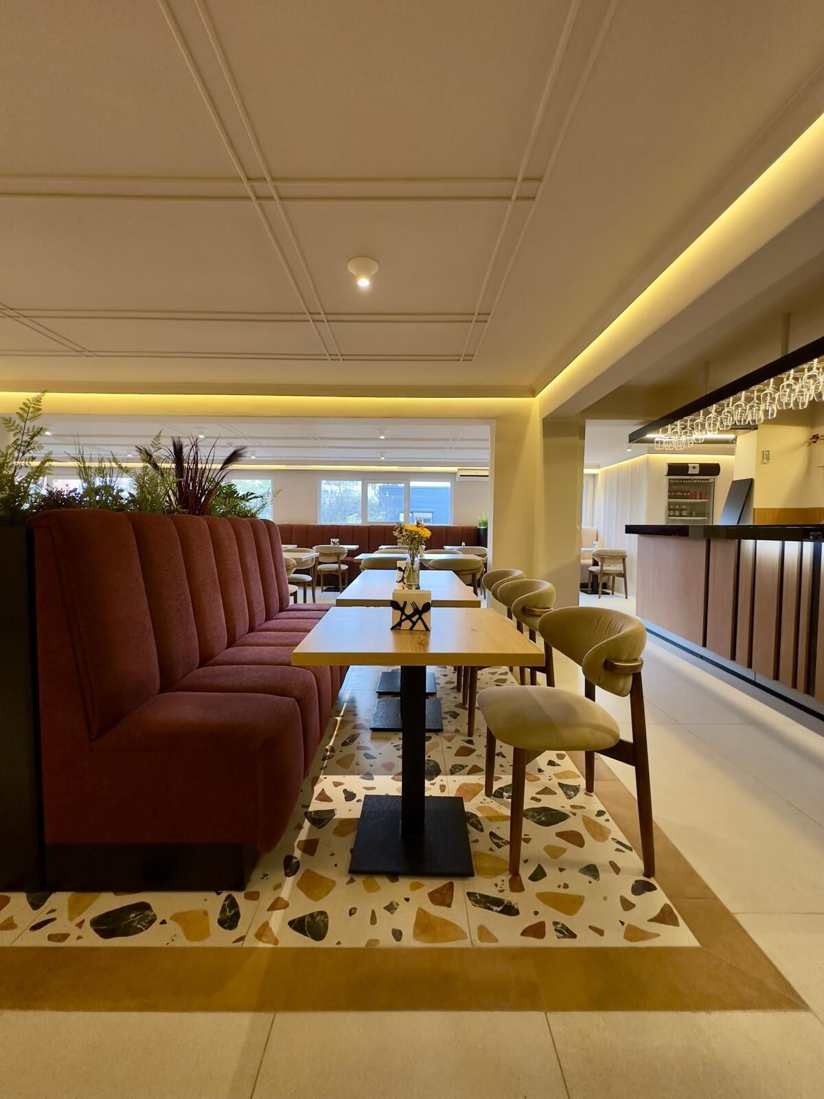 A modern restaurant interior with a long counter, seating area with red and beige chairs, and a patterned floor.