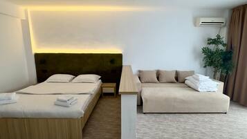 A hotel room with a bed, a sofa, a bedside table, and an air conditioning unit.