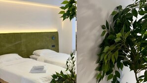 Et hotelværelse med to senge, en grøn sengegavl, en lampe ophængt på væggen og en potteplante.