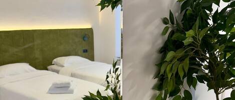 A hotel room with two beds, a green headboard, a wall-mounted light, and a potted plant.