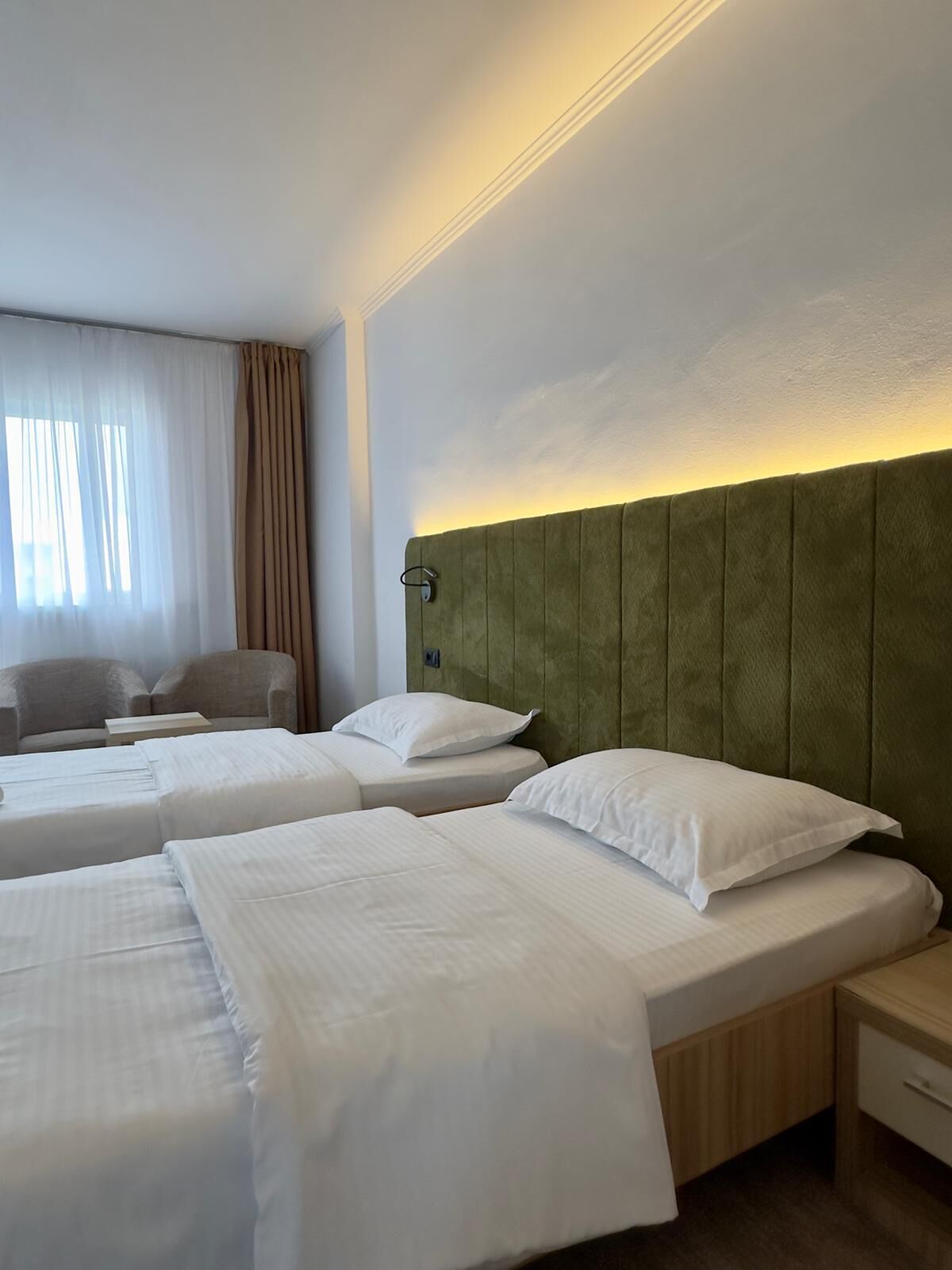 A hotel room with two single beds, a sofa, a small table, and a nightstand.