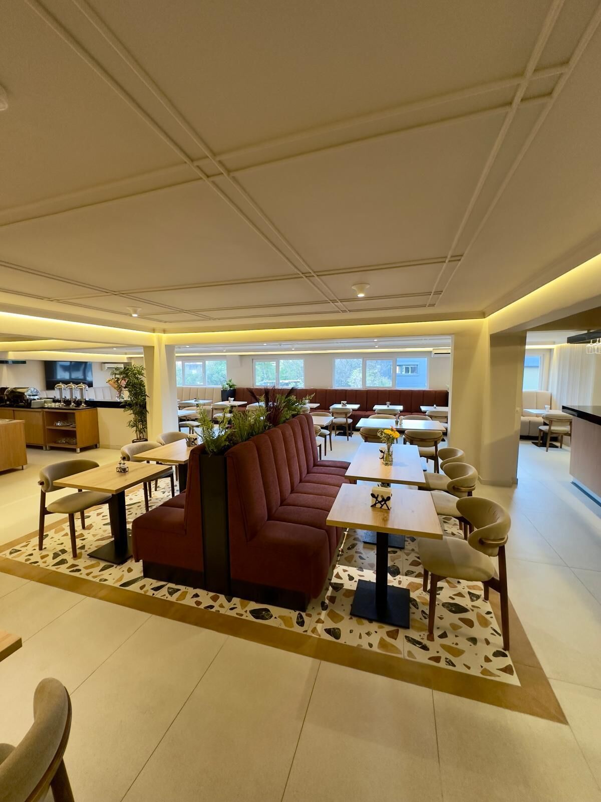 A spacious indoor area with a long red sofa, multiple tables, and chairs arranged for dining or socializing.