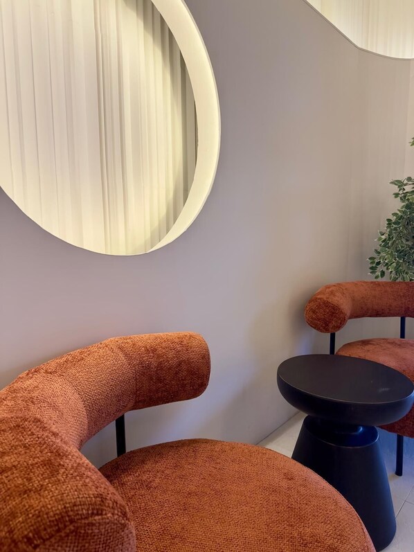 Un intérieur moderne avec un grand miroir rond, des fauteuils recouverts d’un tissu orange et une petite table noire.