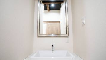 Un baño con un lavamanos blanco rectangular, un espejo con marco de madera y un interruptor de luz en la pared.