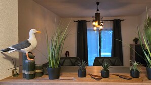 A room with a wooden table, several potted plants, a seagull perched on a post, and a chandelier.