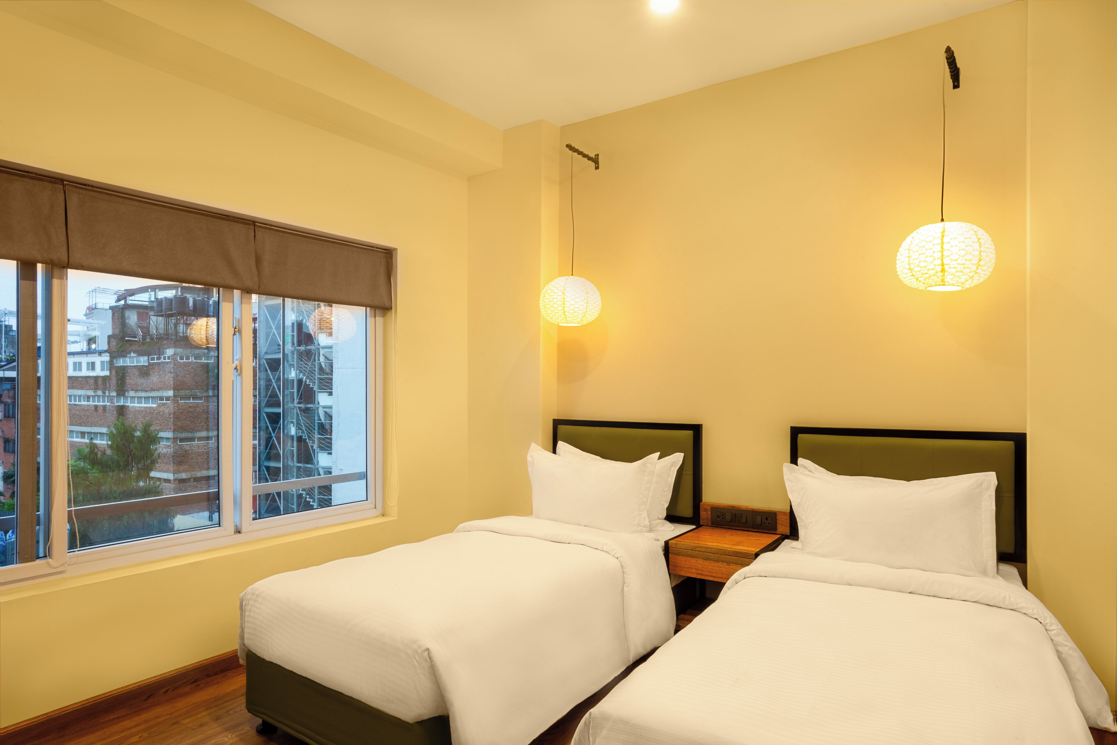 A hotel room with two beds, a large window, and a view of buildings outside.