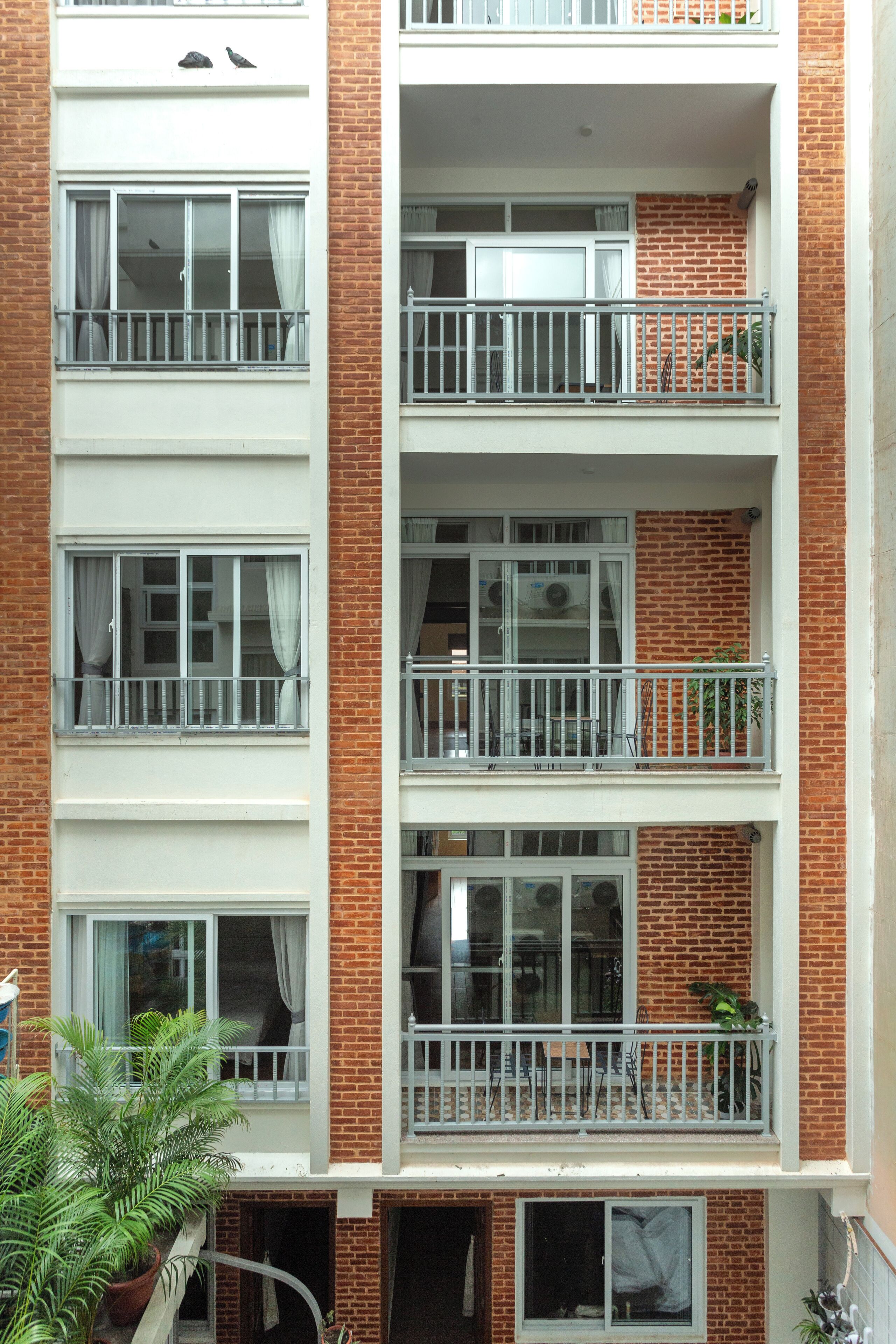 A multi-story residential building with balconies, windows with curtains, and a brick facade.