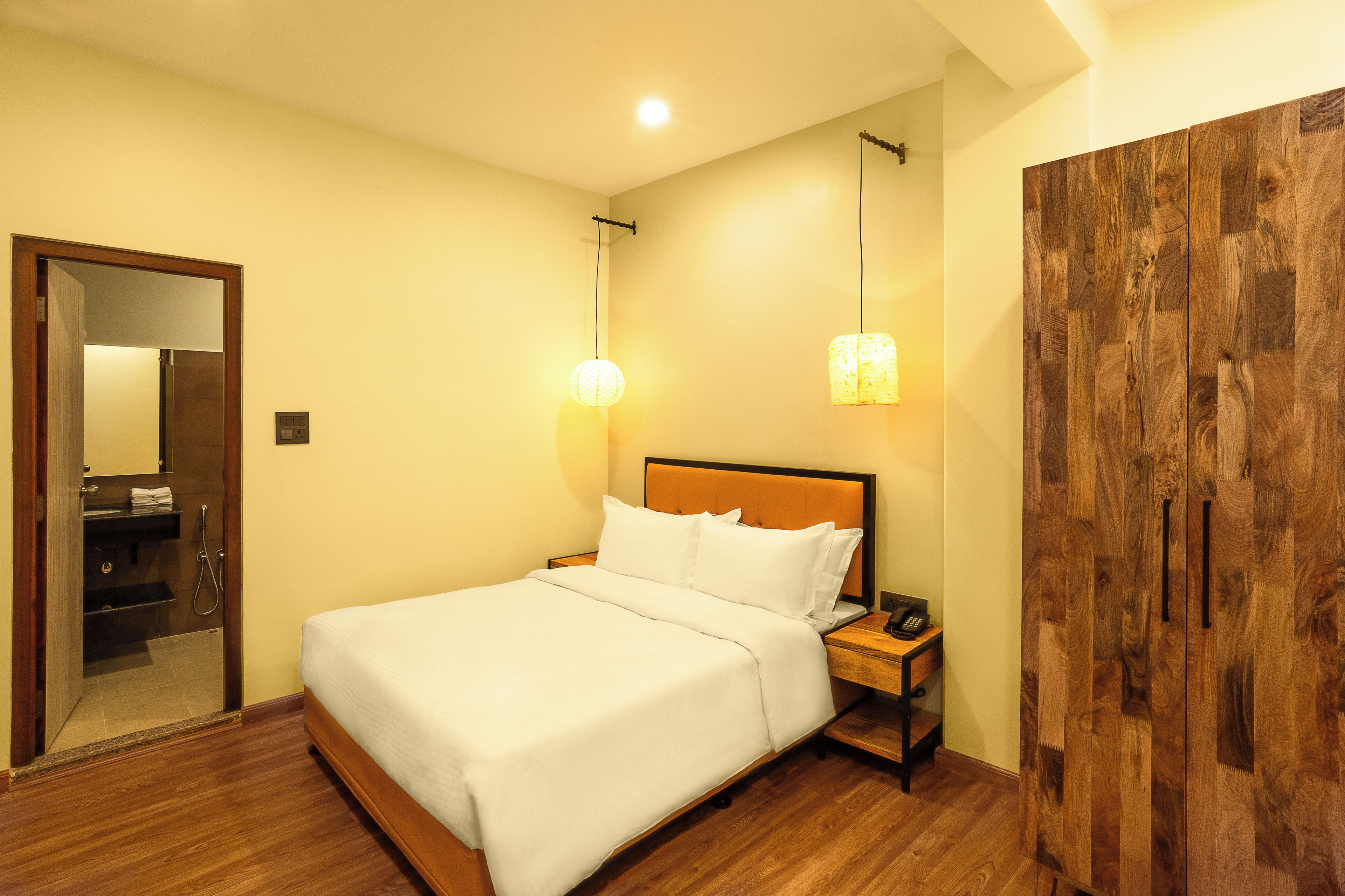 A hotel room with a bed, bedside table, lamp, wardrobe, and a mirror.