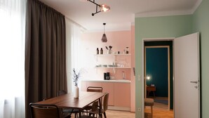 A modern dining area with a wooden table and chairs, a kitchen in the background, and a teal-colored wall. - Apartment in Linz Near Danube Promenade (Linz)