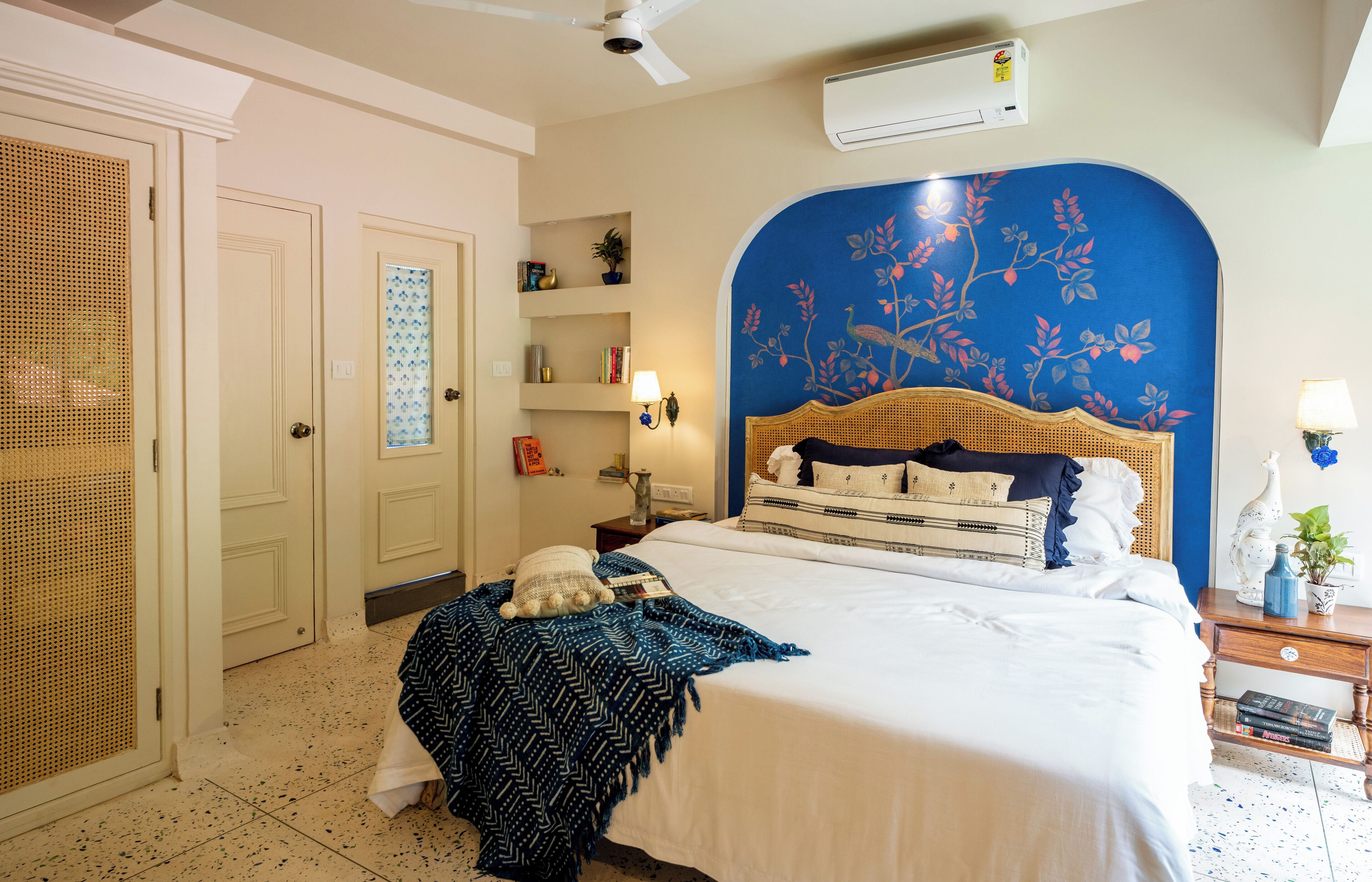 Une chambre à coucher comprenant un lit, une table de chevet, un climatiseur fixé au mur et une porte ornée d’un panneau décoratif.