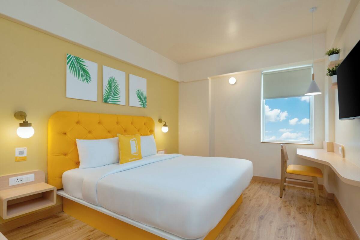 A modern bedroom with a large bed, a desk, and a window with a view of the sky.