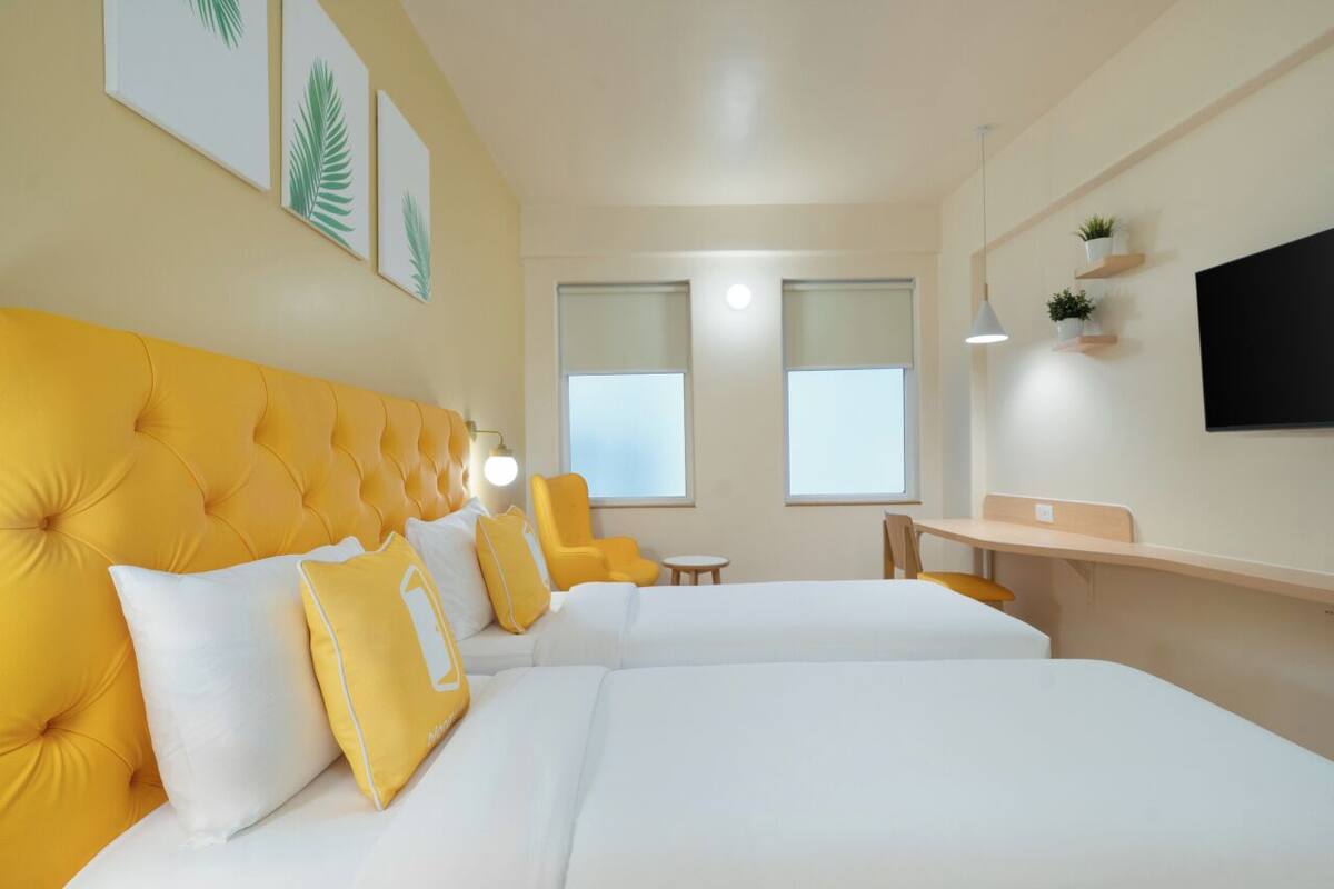 A hotel room with two beds, a desk, and a TV.