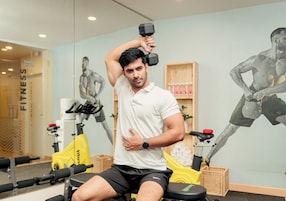 A man exercising with dumbbells in a gym with exercise equipment and a wall mural.