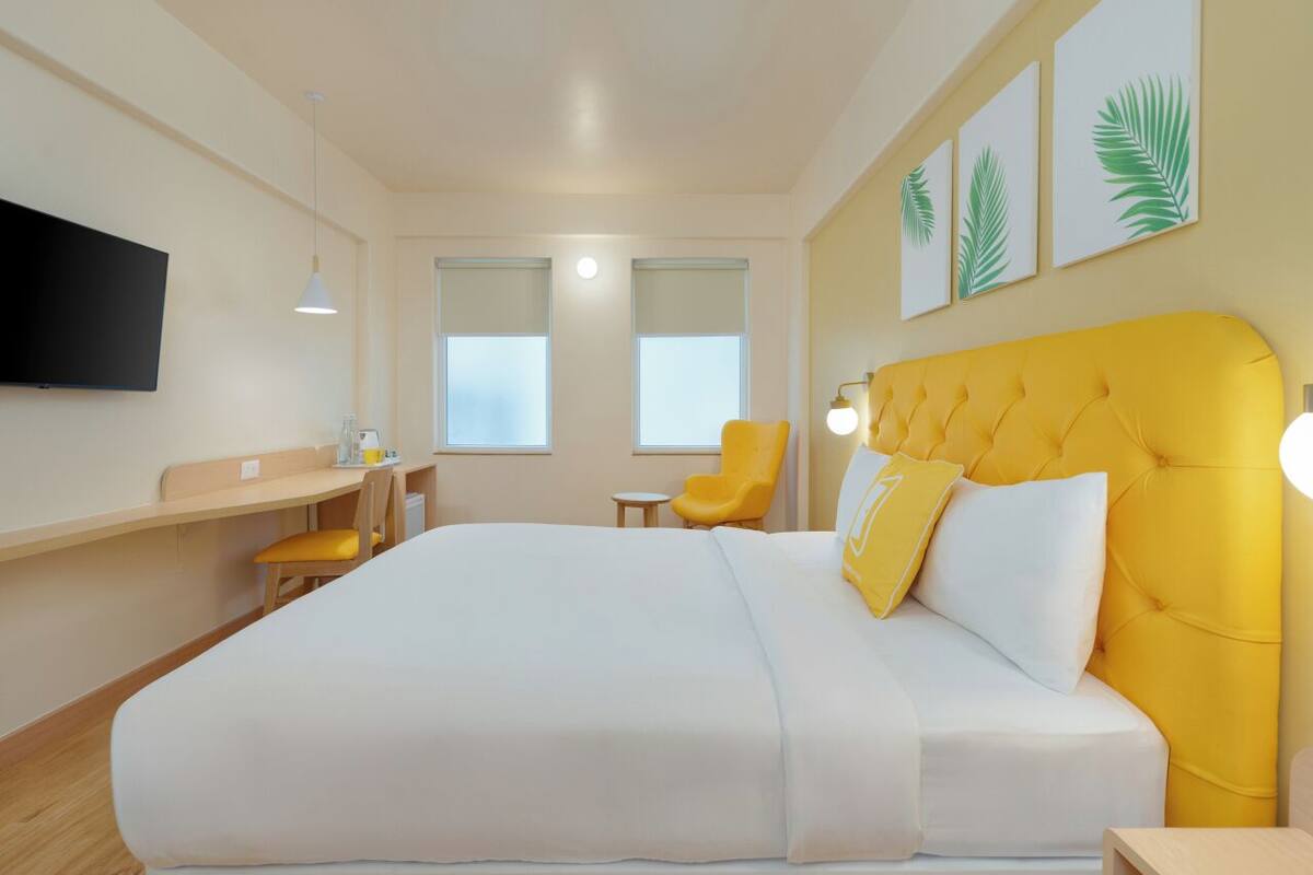 A modern hotel room with a large bed, a desk, a chair, and a TV mounted on the wall.