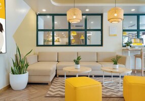 A modern living room with a beige sofa, two round wooden tables, and yellow poufs.