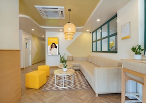 A modern reception area with a sofa, yellow ottomans, a round table with a plant, and a poster on the wall.